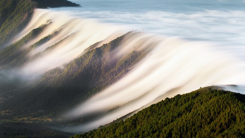 Clouds drift over ridge into valley